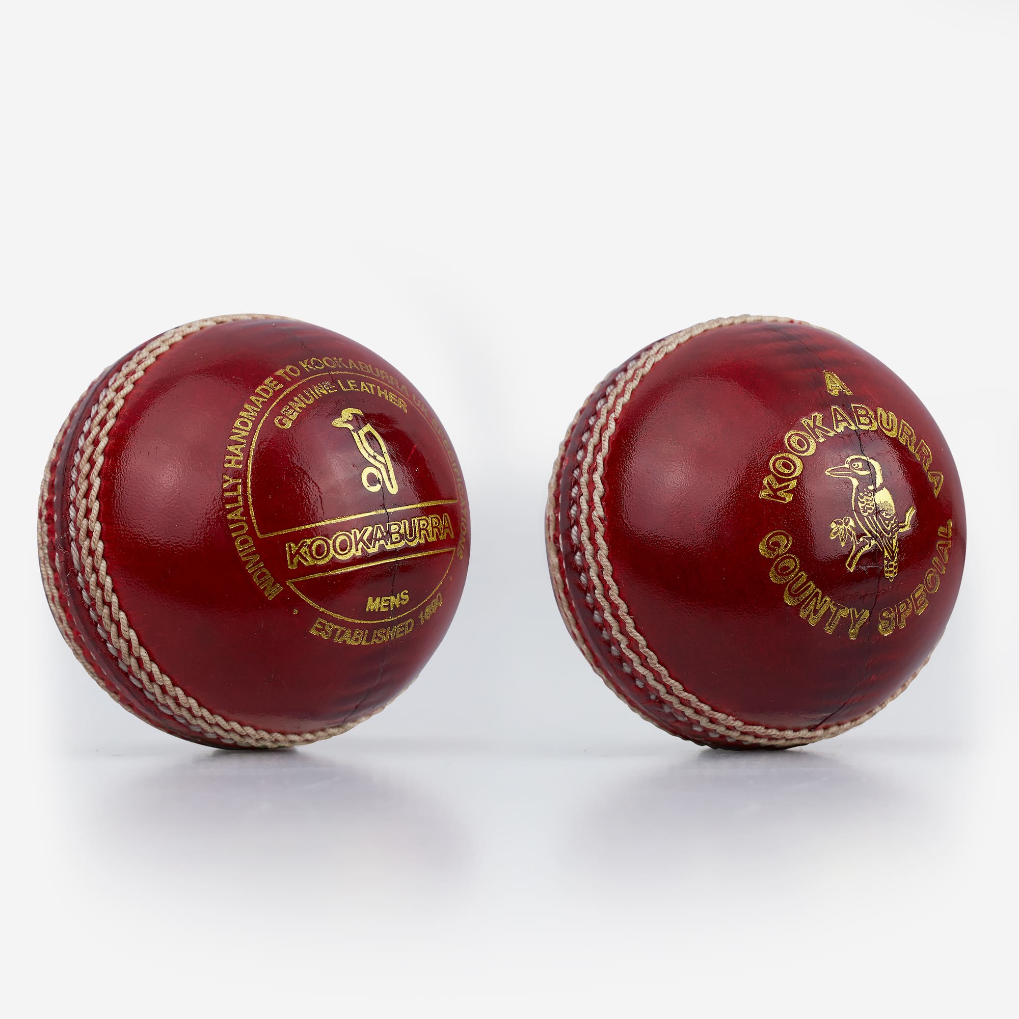 Two Kookaburra County Special red cricket balls positioned to show both the Kookaburra logo and County Special branding, with pronounced linen stitching and a polished leather finish.